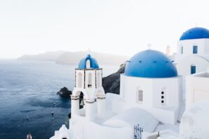Iconic white buildings and blue-domed churches with a bell tower overlooking the sea in Santorini, Greece.